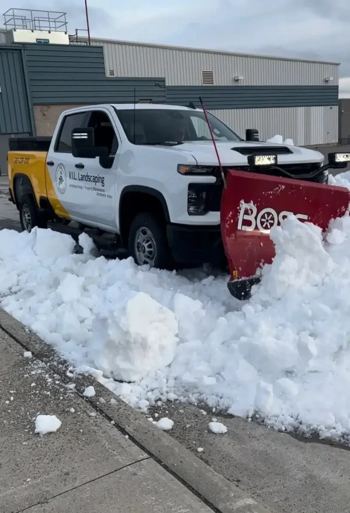V.I.L. Landscaping pickup truck with a snow plow clearing a commercial parking lot