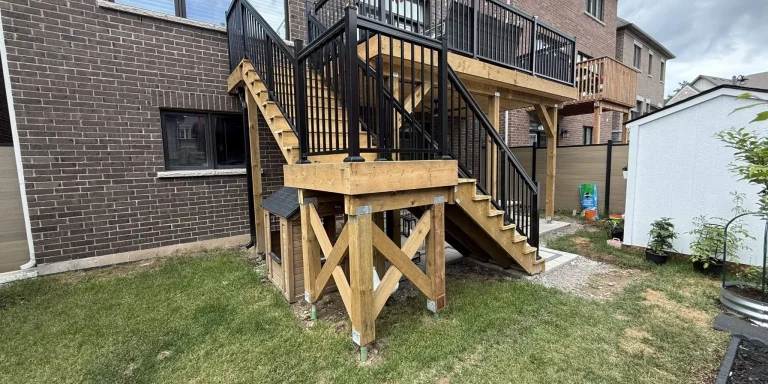 New two-level wood deck with stairs and black aluminum railings behind a brick house