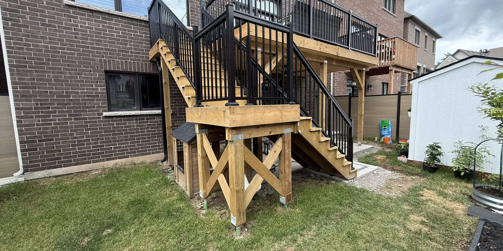 New two-level wood deck with stairs and black aluminum railings behind a brick house in Oakville
