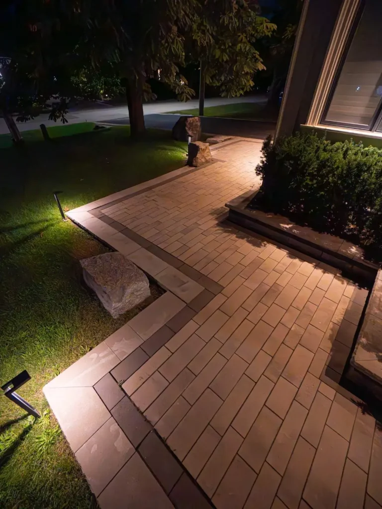Paver walkway at night lit by low-voltage landscape lighting with armour-stone accents
